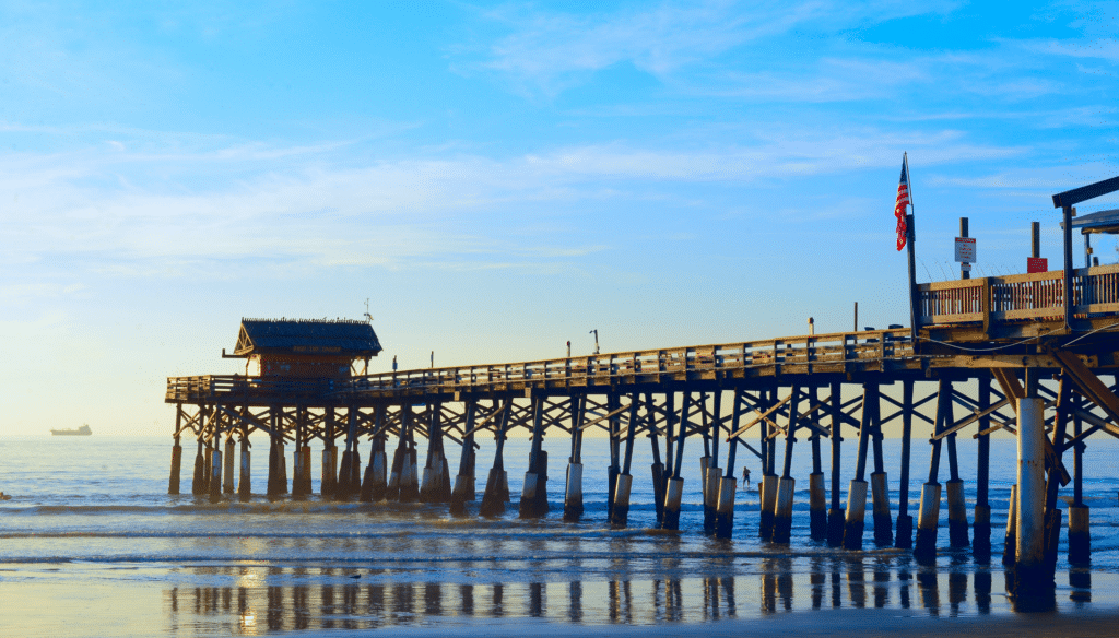 Westgate Cocoa Beach Pier with the sunrise and a ship in the background.