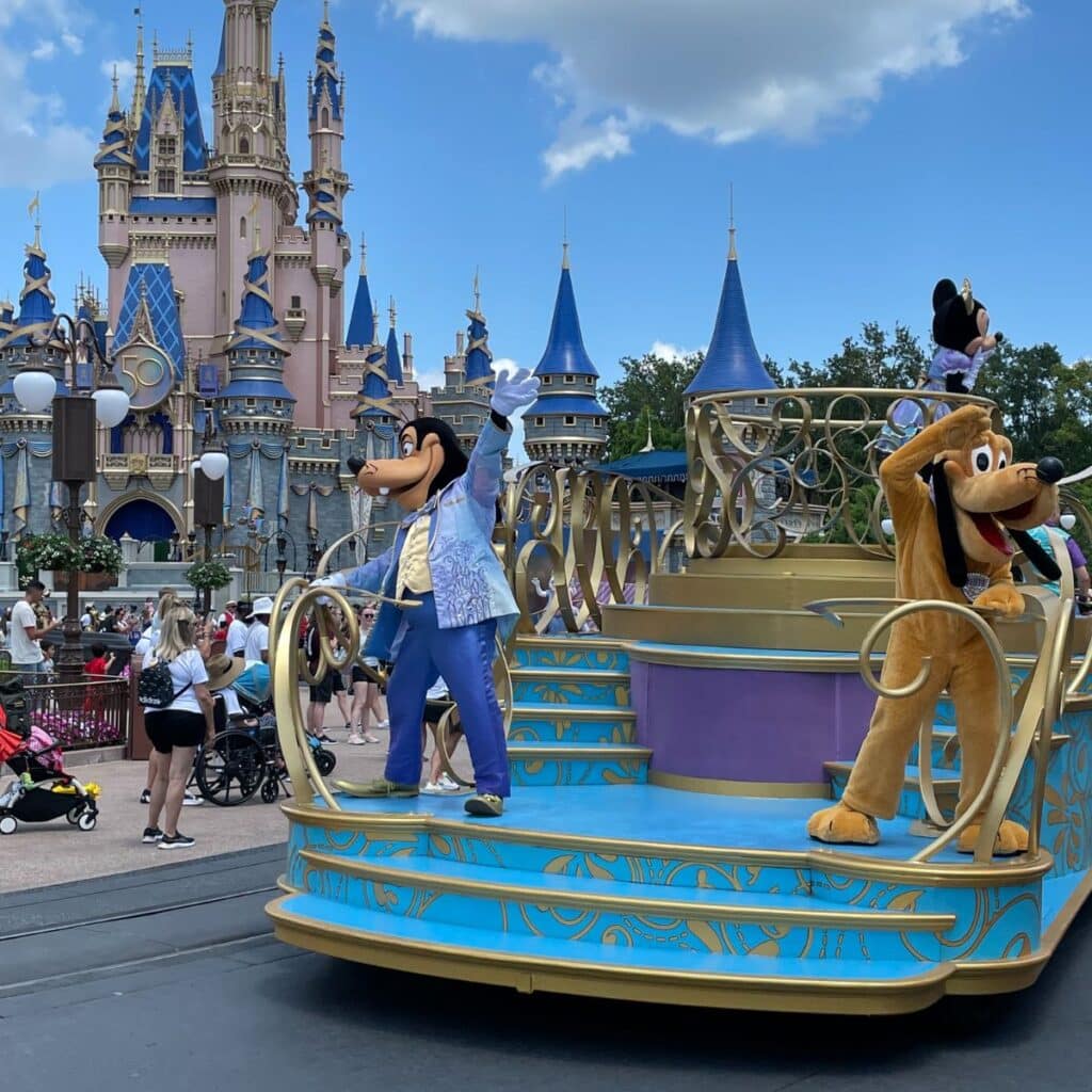 Pluto and Goofy wave from a calvacade float in front of the castle at Magic kingdom